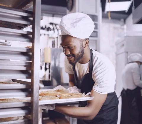 Baker carrying a tray of fresh bread from the racks in a small bakery