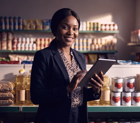Nigerian supermarket manager checking stock on a tablet in front of shelves