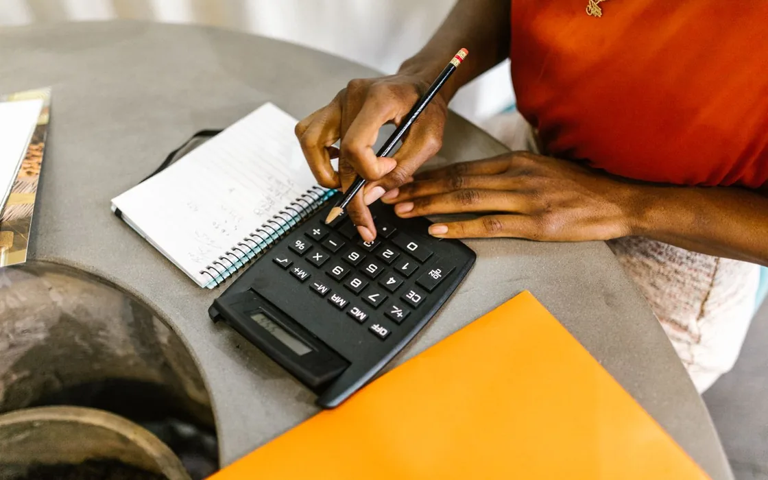 Hands adding up an invoice total on a calculator beside a notebook