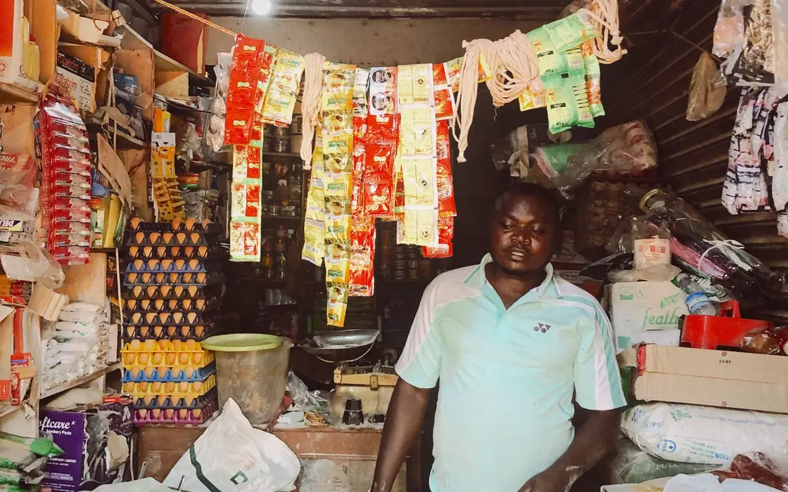 Shopkeeper standing among shelves of stock in a small Nigerian shop